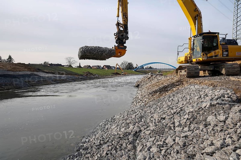 Dinslaken, Voerde, North Rhine-Westphalia, Germany - New Emscher estuary into the Rhine. Restoration of the dykes after dyke erosion during the 2023 flood. An excavator installs gabions and stone baskets on the riverbank. Renaturalisation of the Emscher. Flood protection by expanding the area. The mouth of the Emscher into the Rhine was moved almost 500 metres north from Dinslaken to Voerde. Fish can now swim barrier-free up the new Emscher from the Rhine through a newly created floodplain area. Following the construction of a parallel sewer, the Emscher has been completely free of sewage since January 2022. The river was previously an open, above-ground combined sewer with rainwater and wastewater