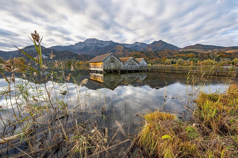 Boathouses in the lake at sunrise, Lake Kochel in autumn with reflection, mountain peaks Herzogstand and Heimgarten in the background, Upper Bavaria, Bavaria, Germany