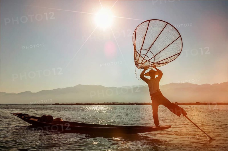 Myanmar travel attraction landmark, Traditional Burmese fisherman at Inle lake, Myanmar famous for their distinctive one legged rowing style on sunset. With light leak and lens flare
