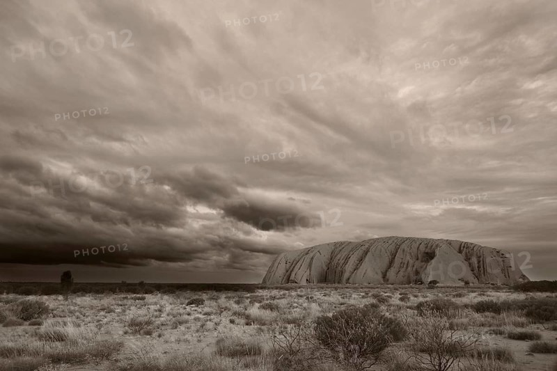 Dark threatening rain clouds hang over Uluru (Ayers Rock), black and white, sepia, monochrome, Australia