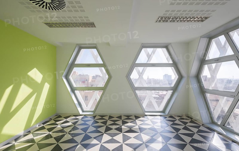 Bright modern auditorium room featuring large hexagonal windows and geometric floor tiles. Natural light casts striking patterns, enhancing the contemporary aesthetic