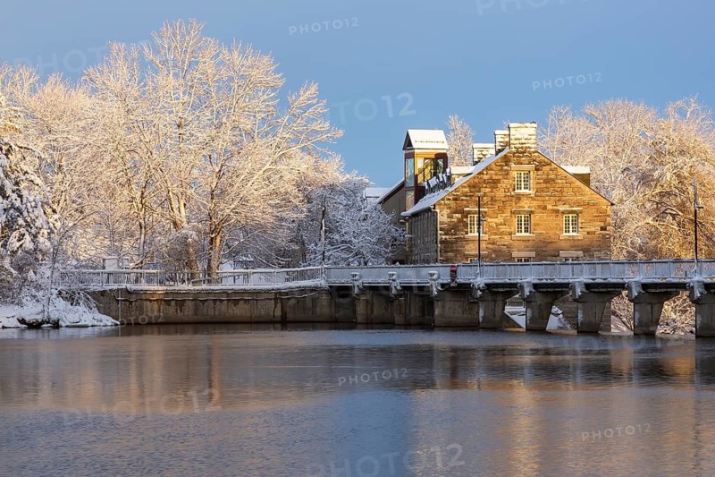 Moulin Neuf water flow control dam and walkway over Des Mille-Iles river plus New Mill on Ile des Moulins with first winter like snow in late autumn at sunset, Old Terrebonne, Quebec, Canada