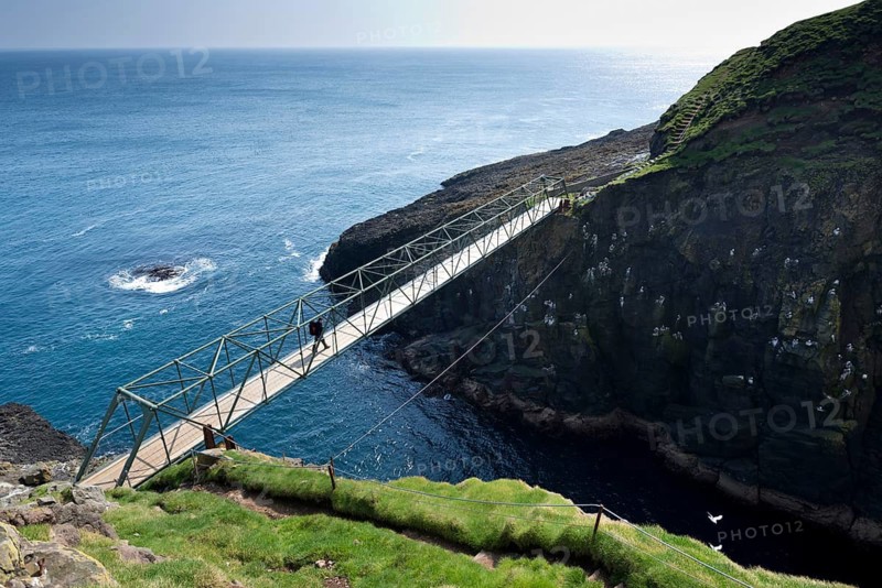 Hiker standing on the so-called Atlantic Bridge, footbridge over a crevice Hólmgjógv, Mykines, Útoyggjar, Faroe Islands, Denmark