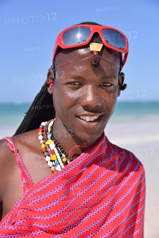 Young Maasai man wearing traditional dress and sunglasses on the beach, Dongwe Beach, Dongwe, Zanzibar, Tanzania