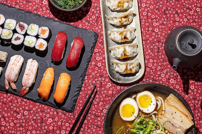 Overhead shot of a Japanese food table with sushi, ramen, dumplings, and tea, captured with strong directional lighting for a vibrant and appetizing look