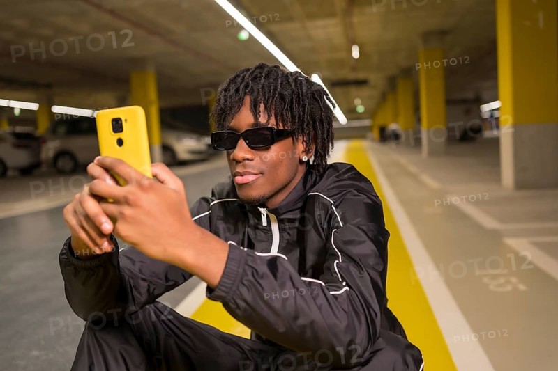 Close-up portrait of an african cool man using phone sitting on a garage