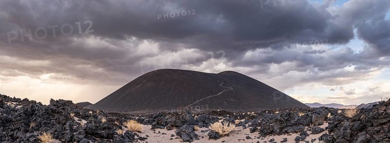 A volcanic hill rises under dramatic clouds in the middle of a rocky desert, Argentina, volcanoes, lava field, Antofagasta