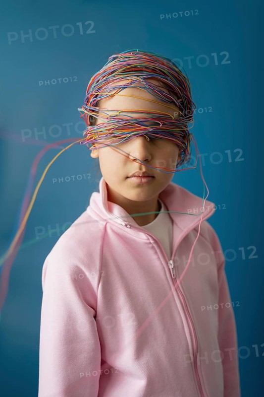 A child with colorful wires wrapped around their head symbolizes the complex and entangling impact of the internet and digital media on today's young generation