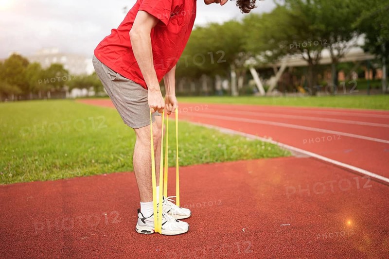 Lower section of an unrecognizable caucasian sportive young man warming up with elastic band in a running track
