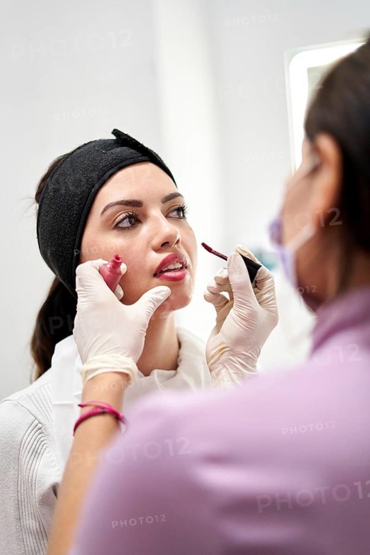 A beauty professional provides makeup application to a client in a modern aesthetic medicine clinic. The focus is on creating a fresh and polished look in a serene environment