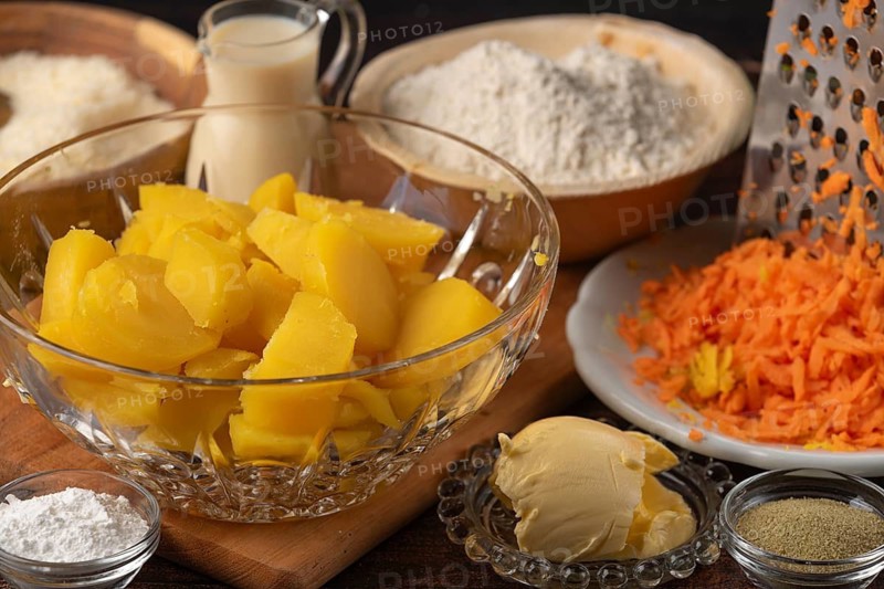 Sliced potatoes and grated carrots next to flour, milk and butter