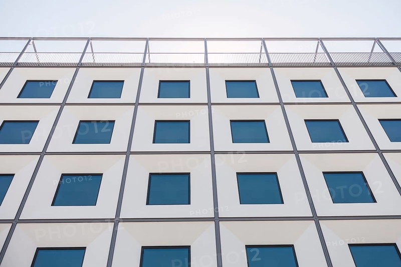 A contemporary building facade with a geometric pattern of windows creates a striking visual effect. The design showcases a combination of modern architectural elements and symmetry
