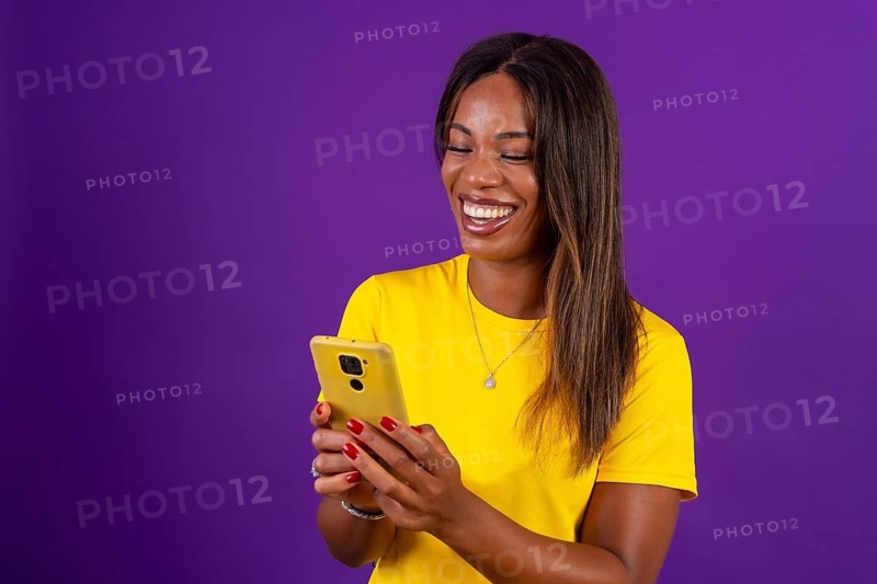 Studio portrait with purple background of a happy african urban woman using mobile phone while smiling