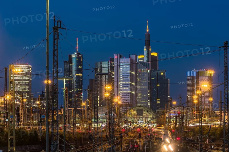View over rails and moving trains to the luminous main station, in the background the colourful skyline of Frankfurt am Main at blue hour, Gallusviertel, Frankfurt am Main, Hesse, Germany