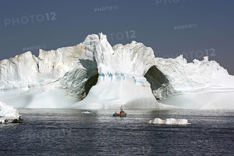 Small fishing boat in front of iceberg with large ice cave, Ilulissat, Disko Bay, Denmark, Greenland