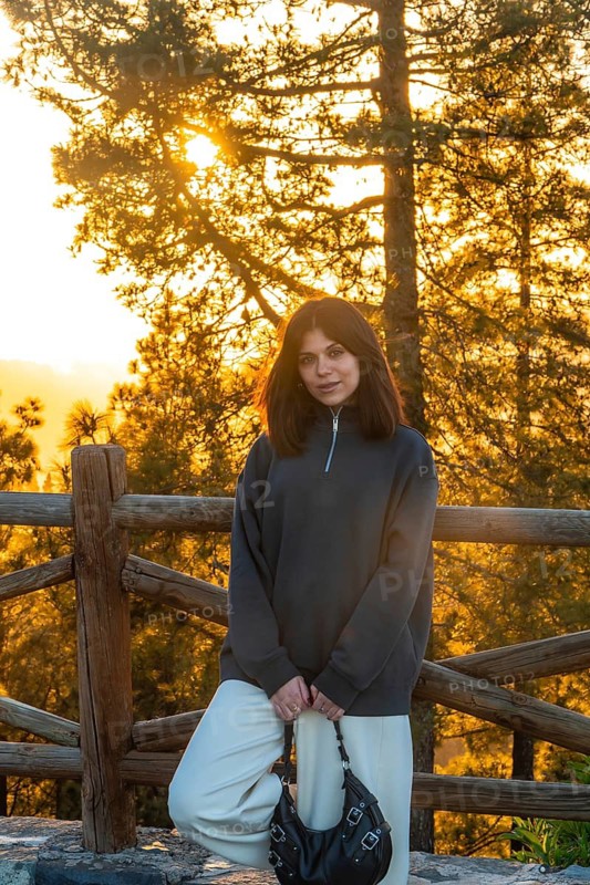 Young woman posing in front of a wooden fence with pine trees and golden sunset light in the forest of moya, gran canaria, spain