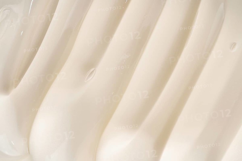 Close-up of a creamy cosmetic gel texture featuring smooth, flowing ridges. The soft beige color and minimalist aesthetic create a soothing, elegant visual