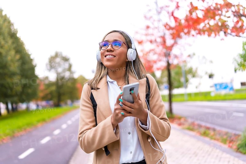 Pretty latin woman using phone and listening to music walking down street