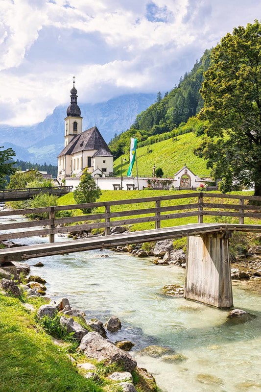 Parish church of St Sebastian by a river in an idyllic Alpine landscape with mountains and forests in the background, bridge, Ramsau, Berchtesgadener Land, Upper Bavaria, Bavaria, Germany