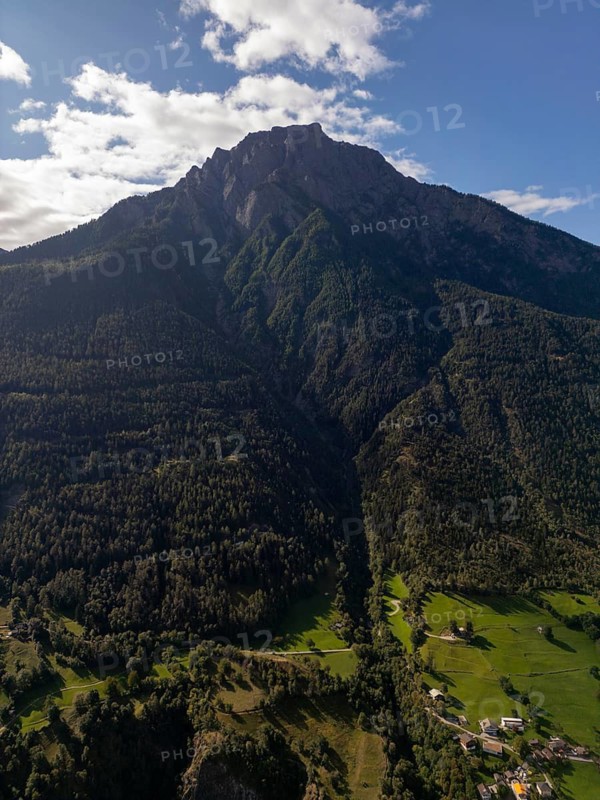 A breathtaking aerial view of the lush, green landscape and towering mountains near Brig, Switzerland. The image captures the serene beauty of a clear sky above the Swiss Alps
