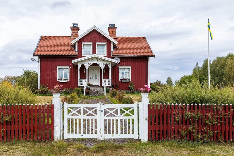 Typical Swedish red house with garden fence and flag pole with Swedish flag, Kalmar län, southern Sweden, Sweden