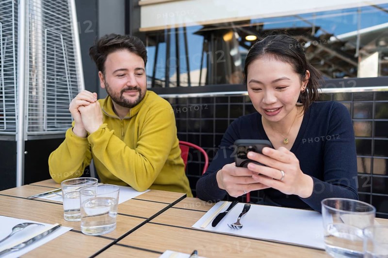 A multiethnic group of friends enjoying their time at an outdoor restaurant, engaging in conversation and looking at a smartphone, showcasing diversity and connection