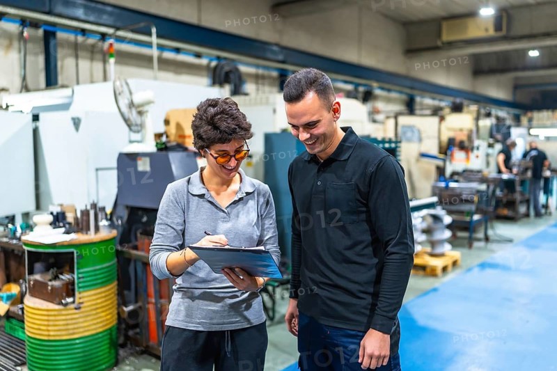 Businesswoman with male caucasian worker talking and inspecting a cnc factory writing notes on clipboard