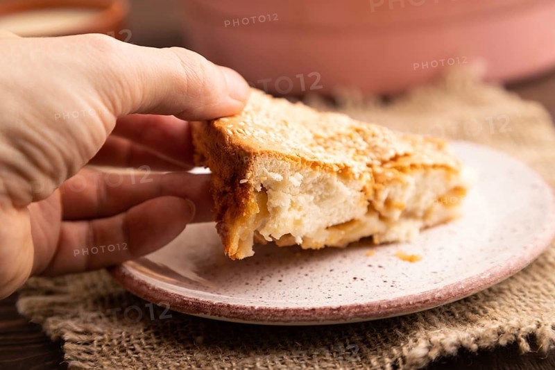 Apple Charlotte cake with hand on brown wooden background and linen textile, cup of milk, side view, close up, selective focus