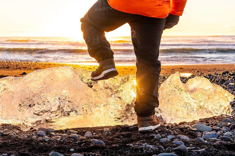 Unrecognizable person at sunrise on Diamond Beach Iceland in winter, resting foot on giant chunk of ice