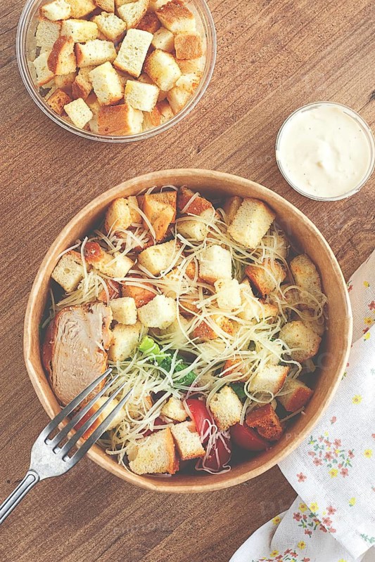 Caesar salad in a paper container, take it on the way, with sauce and croutons, on the table, snack, natural light, no people