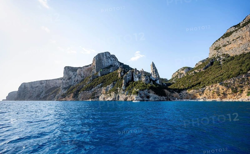 Picturesque rocky coast, cliffs with caves in the morning light, L'Aguglia rock peak, blue sea and Cala Goloritzé beach, Golfo di Orosei, Baunei, Sardinia, Italy