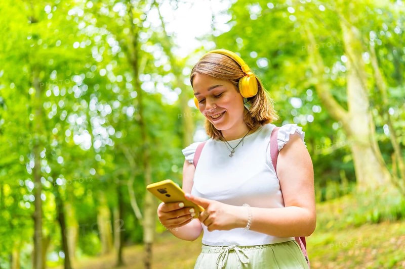Young caucasian female solo traveler listening to music and using phone while hiking in the forest