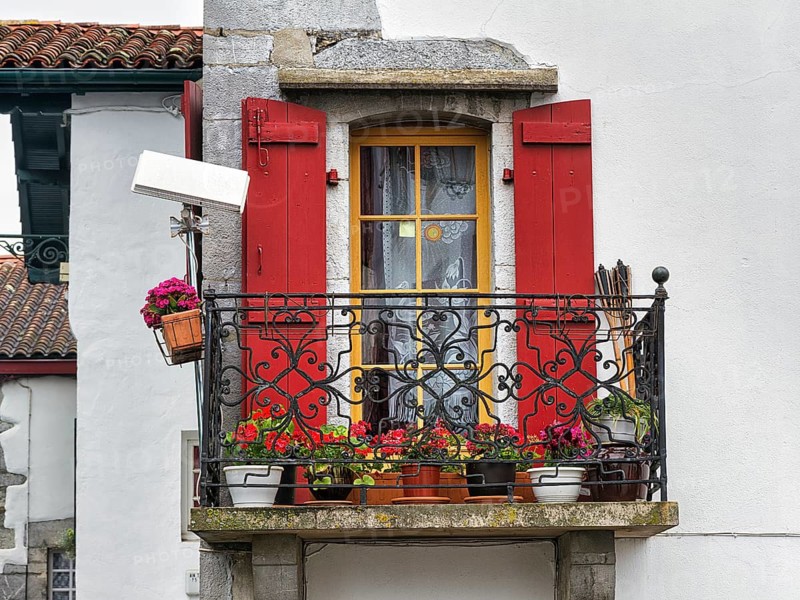 Typical window with balcony, red shutters and potted plants, detail of the façade, Espelette, Département Pyrénées-Atlantiques. Region Nouvelle-Aquitaine, Pays Basque, Basque Country, France