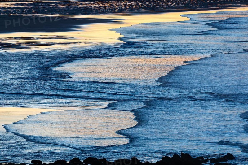 Low tide and gentle waves, at dusk on the North Sea, on the North-east coast of Northumberland, England, UK