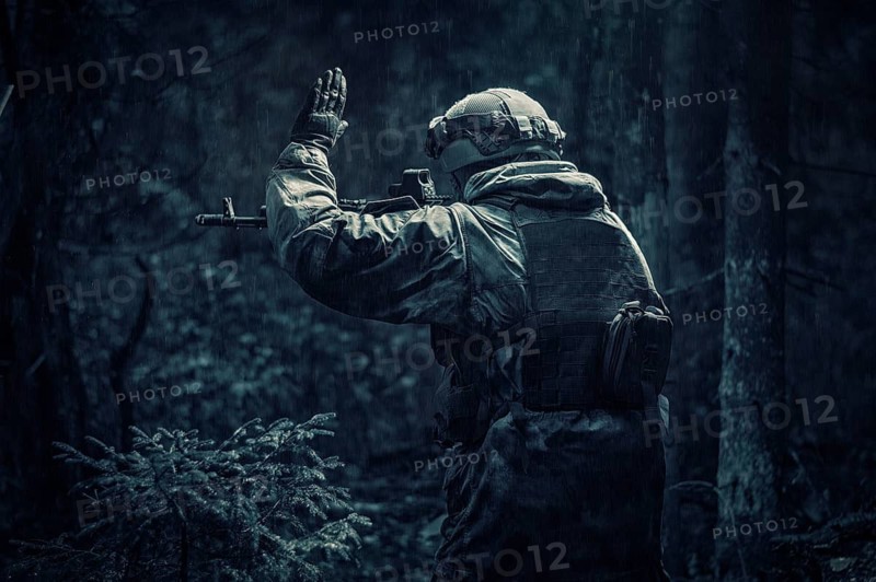 Portrait of a soldier walking through the forest. He raised his hand to warn his partner about the danger. Border Protection Concept. Back view