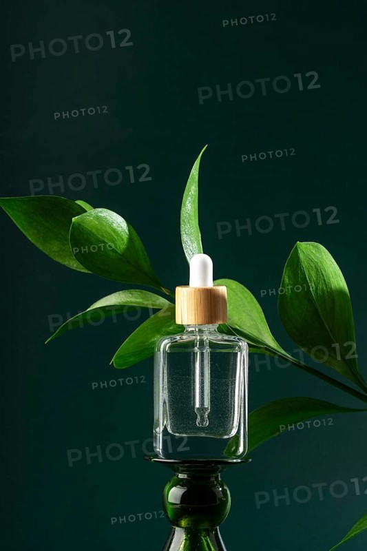 A sleek bottle of transparent micellar water accented with fresh green leaves, featuring a wooden-capped pipette for precise application, ideal for facial skincare routines