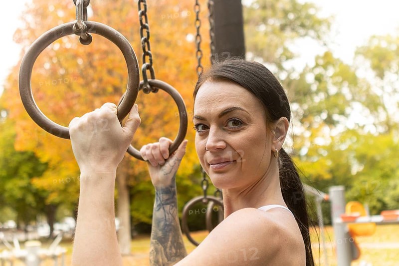 A woman exercises on rings in a New Zealand park during autumn. Surrounded by vibrant fall foliage, she embodies fitness amidst nature colorful backdrop, promoting wellness