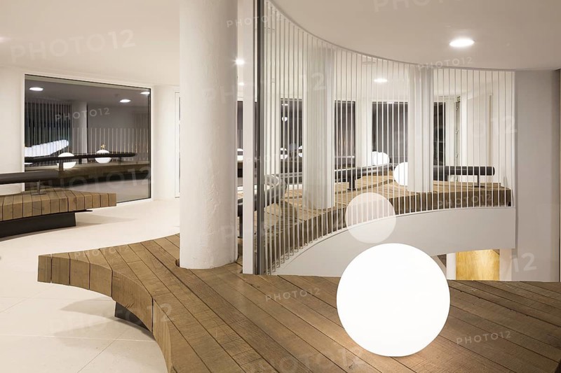 A modern interior lounge in club featuring curved wooden benches, sleek white walls, and ambient lighting. The minimalist design creates a warm, inviting atmosphere with a contemporary flair