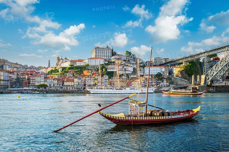 View of Porto city and Douro river with traditional boats with port wine barrels and sailing ship from famous tourist viewpoint Marginal de Gaia riverfront. Porto, Vila Nova de Gaia, Portugal