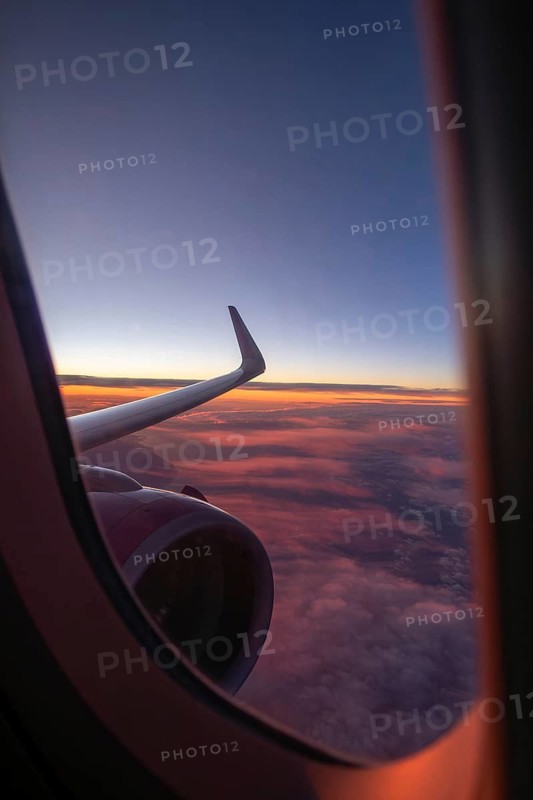A stunning view from an airplane window captures the vibrant colors of a sunset over a cloudscape, with the sleek wing slicing through the sky, enhancing a sense of adventure