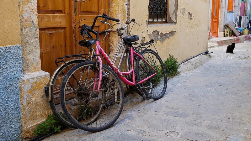 Two old bicycles standing against a yellow wall in a narrow street of the old town, Symi Town, Symi, Dodecanese, Greek Islands, Greece