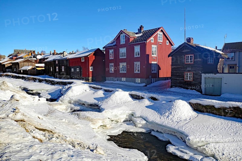 Snowy landscape with red and brown wooden houses by a frozen river under a clear sky, Røros, mining town, Unesco World Heritage Site, Tröndelag, Norway