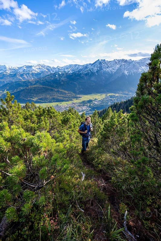 Mountaineer on a narrow hiking trail between mountain pines, view of Garmisch-Partenkirchen and mountain panorama, hike to Kramerspitz, in autumn, Ammergau Alps, in autumn, Bavarian Alps, Bavaria, Germany