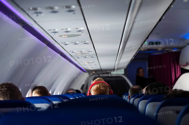 Interior view of a modern airplane cabin with passenger with red headphones seated and blue ambient lighting during a commercial flight