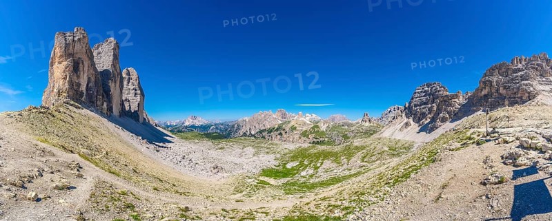 Panoramic view of the tre cime di lavaredo hiking trail in summer, featuring the iconic peaks, clear blue sky, and lush green valleys of the dolomites in italy