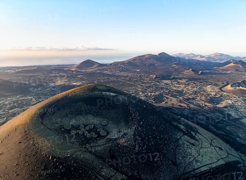 Picturesque volcanic landscape with volcanic craters and lava fields in morning light, Montaña Negra volcano, Los Volcanes Natural Park, aerial view, Lanzarote, Canary Islands, Spain