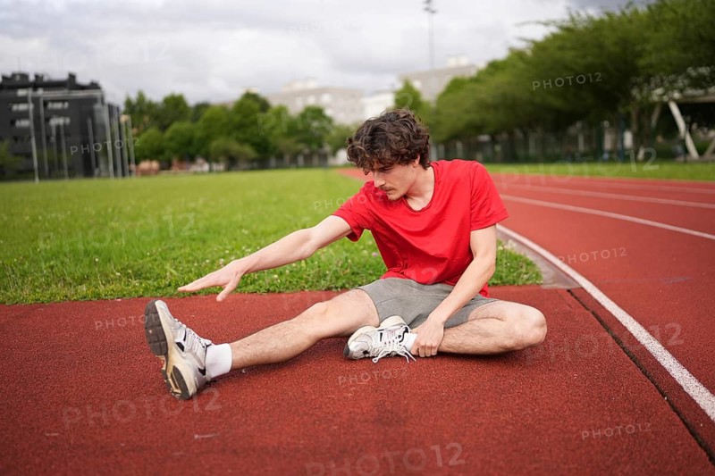 Full length photo of a caucasian young sportive man warming up stretching legs in an outdoor running track