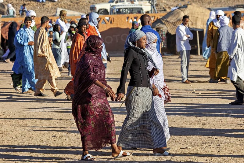 A lively scene at a market with many people in traditional costumes, veiled woman at the Tamanrasett Festival in the Sahara in Algeria