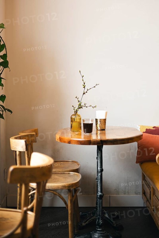 A cozy cafe corner featuring a wooden table with a decorative vase and drinks, surrounded by wooden chairs. Soft natural light creates a warm, inviting ambiance