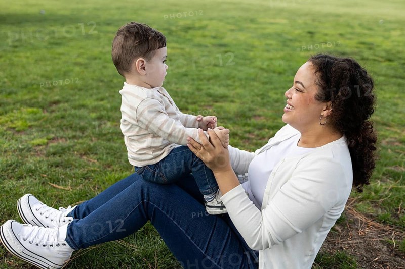 A joyful scene of a mother and her baby enjoying a playful moment in the park. The mother sits on the grass, holding her child, creating a tender, loving atmosphere